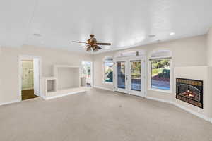 Unfurnished living room featuring carpet, french doors, a glass covered fireplace, ceiling fan, and baseboards