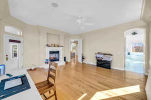 Interior space with arched walkways, light wood-style flooring, a ceiling fan, baseboards, and a glass covered fireplace