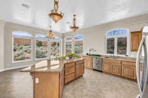 Kitchen with light stone counters, decorative light fixtures, light tile patterned floors, appliances with stainless steel finishes, and a kitchen island