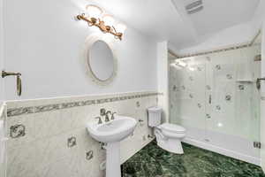 Bathroom featuring a stall shower, visible vents, toilet, a wainscoted wall, and tile walls