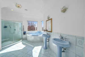 Full bath with tile walls, a stall shower, wainscoting, tile patterned flooring, and a bath