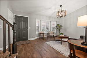 Foyer entrance with baseboards, stairway, dark wood-style flooring, and a notable chandelier