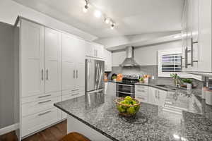 Kitchen with lofted ceiling, stainless steel appliances, a peninsula, a sink, and wall chimney exhaust hood