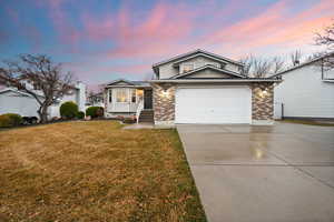 View of front of house with concrete driveway, brick siding, a front lawn, and an attached garage