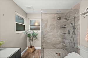 Full bathroom with visible vents, toilet, a stall shower, wood finished floors, and baseboards