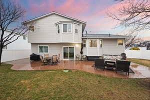 Back of property at dusk featuring a fenced backyard, a patio, and a lawn