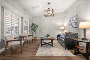 Living area with lofted ceiling, an inviting chandelier, baseboards, and wood finished floors