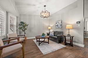 Living area featuring vaulted ceiling, a notable chandelier, baseboards, and wood finished floors