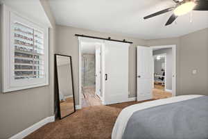 Bedroom with ceiling fan, a barn door, carpet flooring, and baseboards