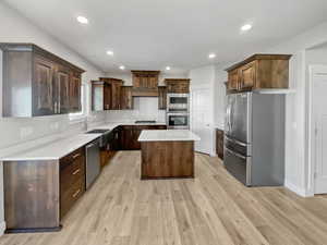 Kitchen with light countertops, appliances with stainless steel finishes, light wood-style floors, dark brown cabinetry, and a kitchen island