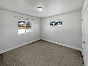 Carpeted spare room featuring a textured ceiling, visible vents, and baseboards