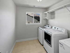 Washroom featuring washing machine and clothes dryer, light tile patterned floors, visible vents, laundry area, and baseboards