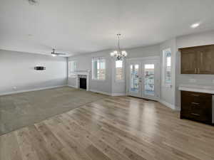 Unfurnished living room featuring ceiling fan with notable chandelier, a fireplace, baseboards, french doors, and light wood finished floors