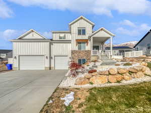 View of front of house with driveway, stone siding, an attached garage, and board and batten siding