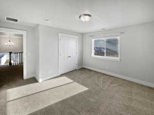 Unfurnished bedroom with carpet floors, visible vents, baseboards, and an inviting chandelier