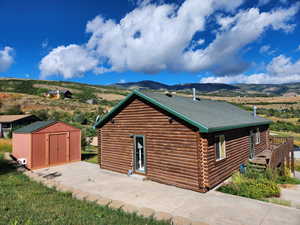 View of side of home featuring an outbuilding, roof with shingles, a storage shed, a mountain view, and log exterior