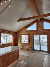 Kitchen with rustic walls, rail lighting, light wood-style floors, high vaulted ceiling, and beam ceiling