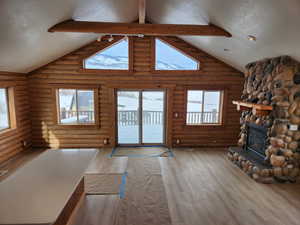 Unfurnished living room with a fireplace, a textured ceiling, wood finished floors, high vaulted ceiling, and beamed ceiling