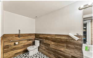 Half bath featuring toilet, a wainscoted wall, visible vents, and wood walls