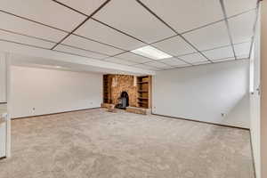 Finished below grade area with built in shelves, carpet, a paneled ceiling, a wood stove, and baseboards