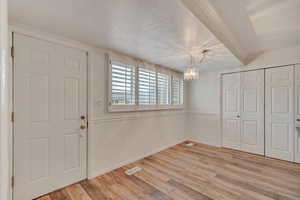 Entrance in kitchen featuring new light wood finished floors, visible vents, a wainscoted wall, an inviting chandelier, and a textured ceiling