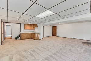 Kitchenette featuring a drop ceiling, light colored carpet, open floor plan, light countertops, and brown cabinetry