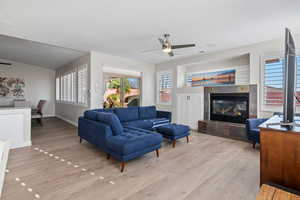 Living area featuring ceiling fan, a tiled fireplace, wood finished floors, and baseboards