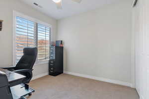 Carpeted office space with a ceiling fan, visible vents, and baseboards