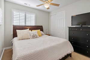 Carpeted bedroom featuring ceiling fan, a closet, visible vents, and baseboards