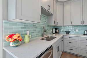 Kitchen featuring light stone counters, backsplash, wood finished floors, a sink, and stainless steel dishwasher