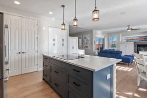 Kitchen with a fireplace, black electric stovetop, gray cabinets, light wood-type flooring, and stainless steel fridge