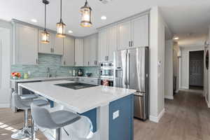 Kitchen with stainless steel appliances, tasteful backsplash, light wood-style flooring, and a kitchen breakfast bar