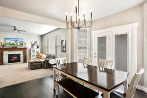 Dining space featuring a textured ceiling, ceiling fan with notable chandelier, a tiled fireplace, and dark wood finished floors