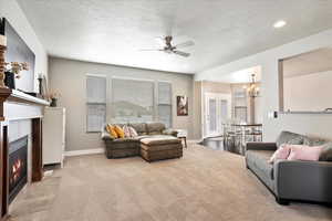 Carpeted living area featuring ceiling fan with notable chandelier, a textured ceiling, a fireplace with flush hearth, and baseboards