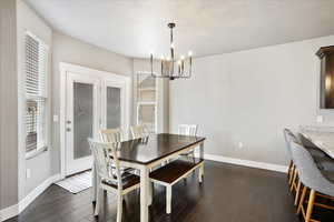 Dining space with dark wood-style flooring, a textured ceiling, baseboards, and an inviting chandelier