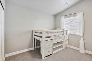 Bedroom with light carpet, baseboards, visible vents, vaulted ceiling, and a textured ceiling