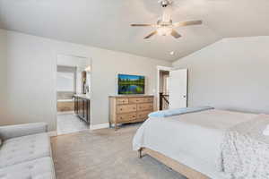 Bedroom featuring lofted ceiling, ensuite bathroom, light colored carpet, a ceiling fan, and baseboards