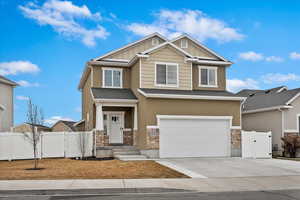 Craftsman-style house with driveway, stone siding, a gate, fence, and board and batten siding