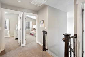 Hall with carpet, baseboards, visible vents, and an upstairs landing