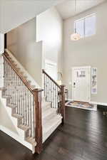 Foyer entrance featuring dark wood-type flooring, stairway, a towering ceiling, and baseboards