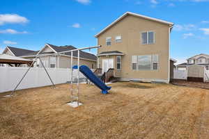 Rear view of property featuring a playground, a fenced backyard, and stucco siding