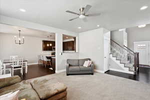 Living area with stairs, recessed lighting, dark wood-type flooring, baseboards, and ceiling fan with notable chandelier