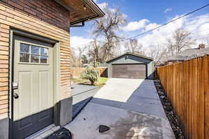 View of side of home featuring a garage, brick siding, fence, and an outbuilding