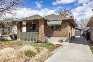 Bungalow with an outbuilding, covered porch, brick siding, a detached garage, and a chimney