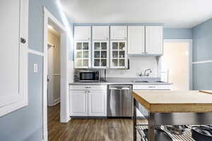 Kitchen with dark wood finished floors, decorative backsplash, white cabinets, appliances with stainless steel finishes, and a sink