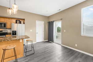 Kitchen with a kitchen bar, tasteful backsplash, appliances with stainless steel finishes, wood finished floors, and baseboards