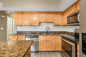 Kitchen featuring a sink, appliances with stainless steel finishes, backsplash, light wood finished floors, and dark stone countertops