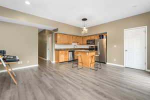 Kitchen with light wood finished floors, appliances with stainless steel finishes, a breakfast bar area, and baseboards