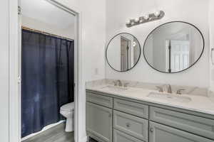 Bathroom featuring double vanity, toilet, a sink, and wood finished floors