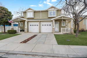 Craftsman-style house featuring covered porch, stone siding, a front lawn, and concrete driveway